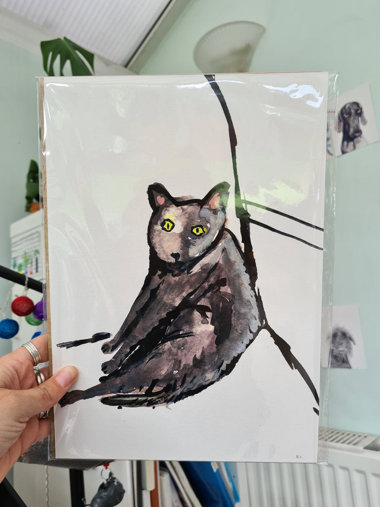 Watercolor painting of a gray cat with bright yellow eyes sitting in a relaxed, slouched position against a simple black line background on white paper.