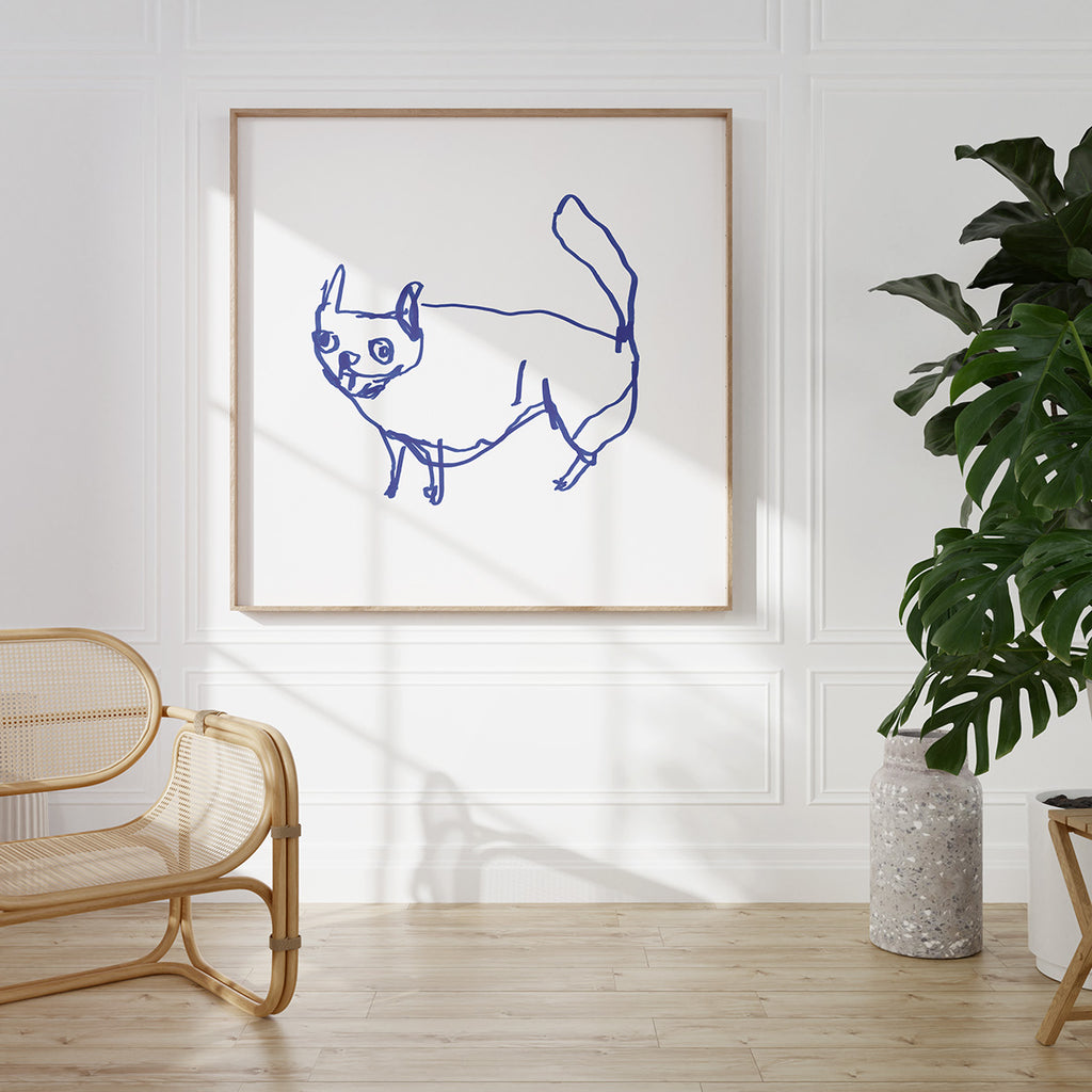 Minimalist interior featuring a large framed line drawing of a dog in bold blue on a white canvas, hung on a white paneled wall. The space includes a rattan bench, a terrazzo-style plant pot with a large monstera plant, and wooden flooring with natural light streaming in.